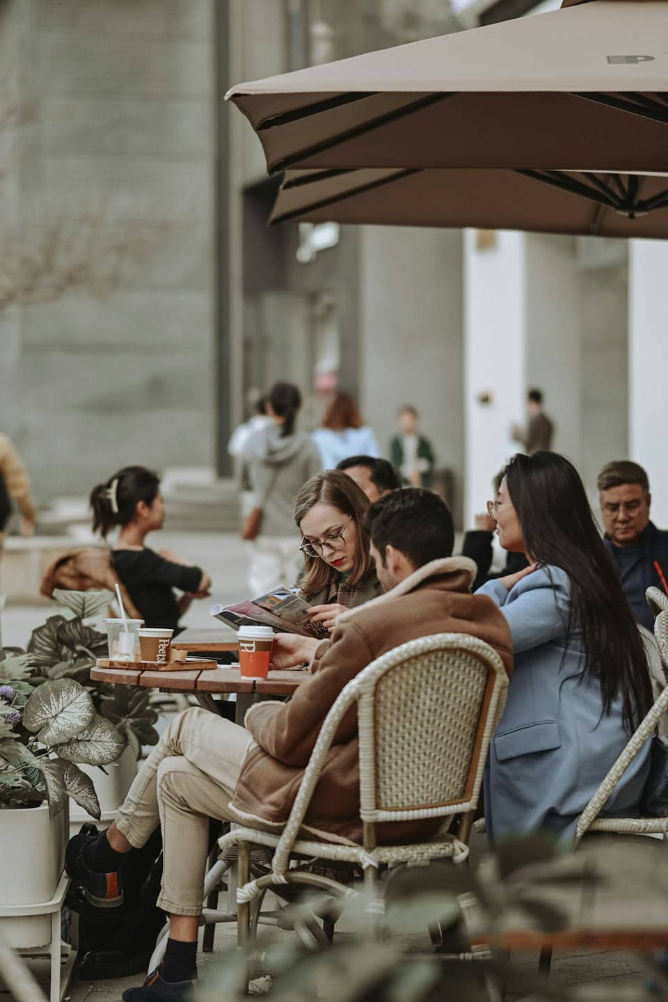 People converse and read at an outdoor cafe table.