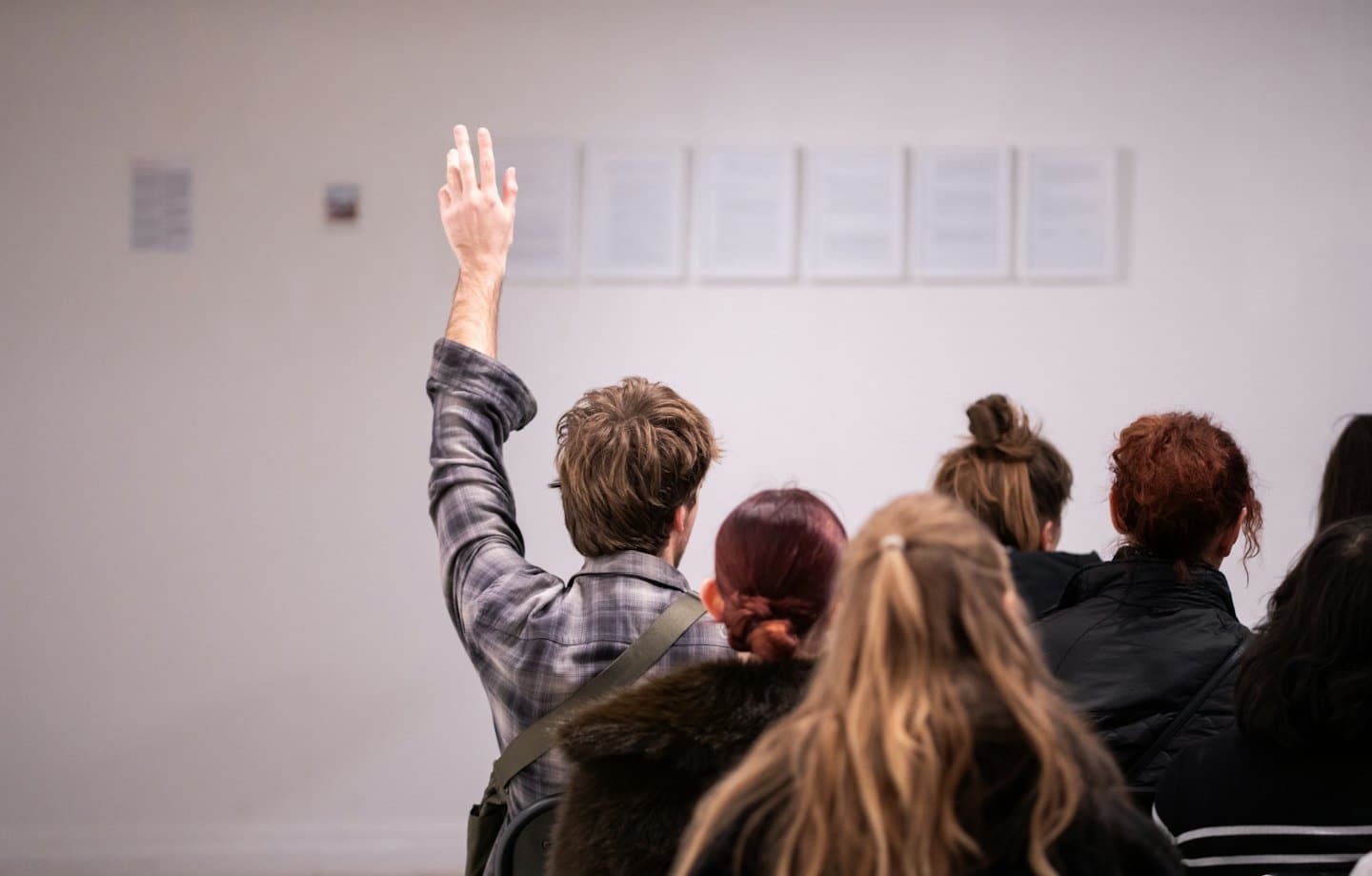 Attendees at a meeting, one raising hand to speak.