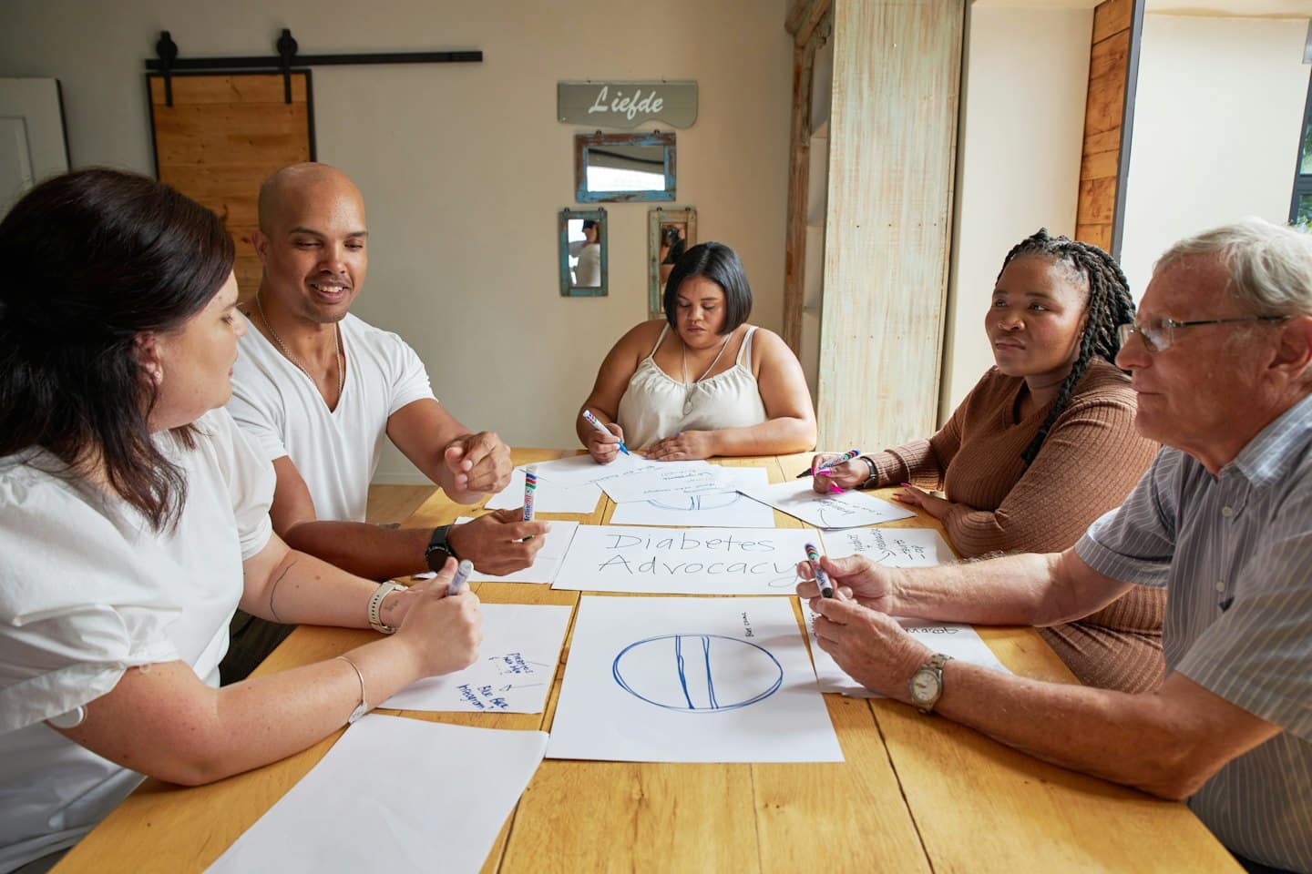 Diverse adults collaborating around a table with 'Diabetes Advocacy' papers.