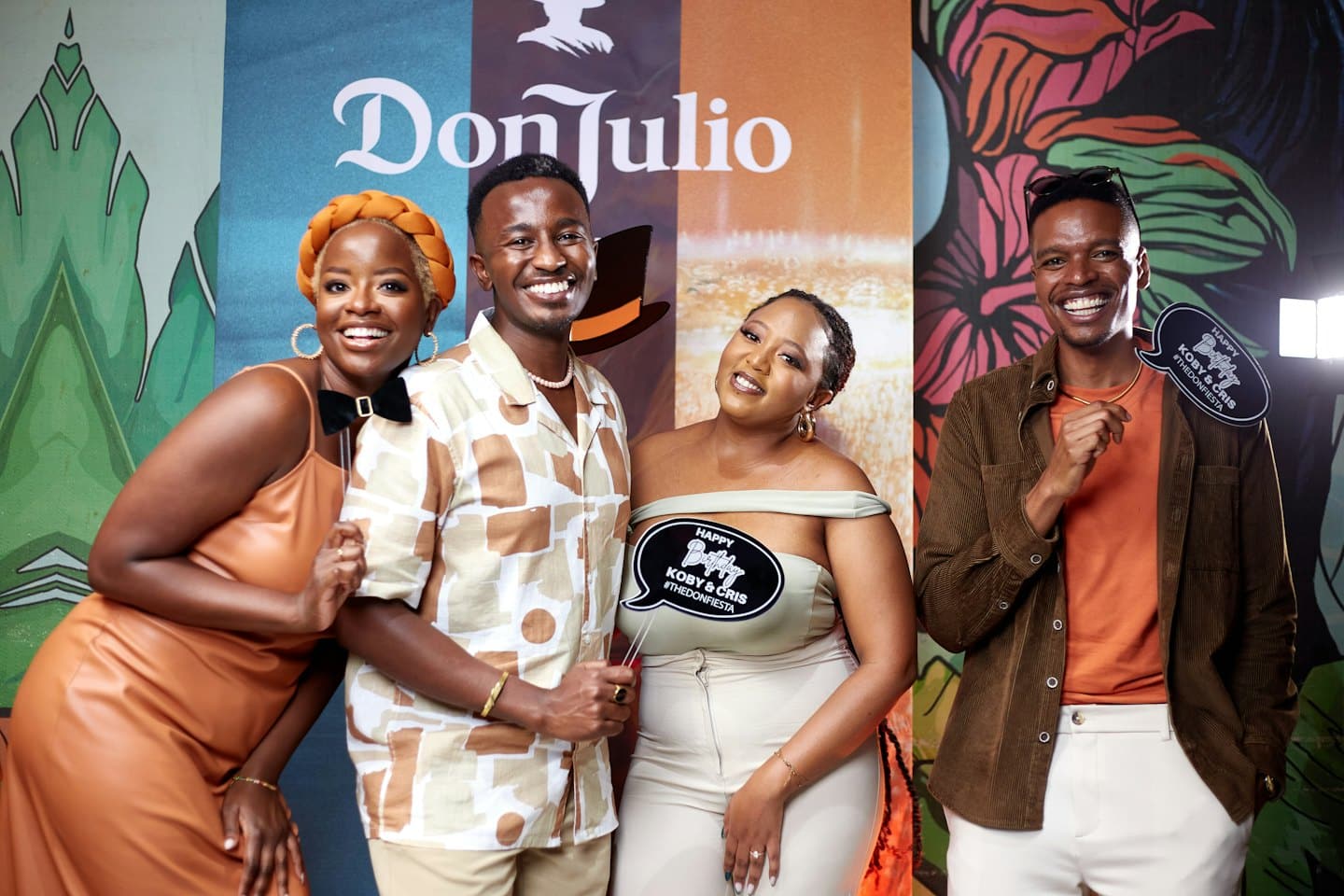 Four adults pose with props in front of a backdrop.