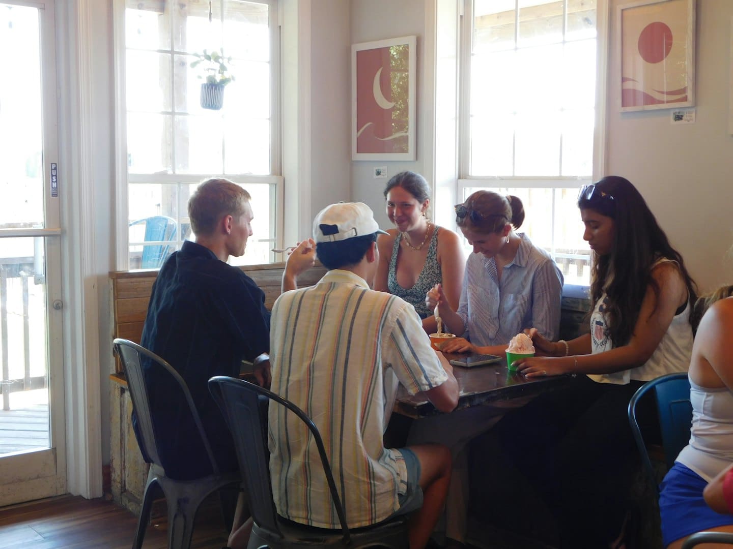 Friends eating desserts and talking at a wooden cafe table.